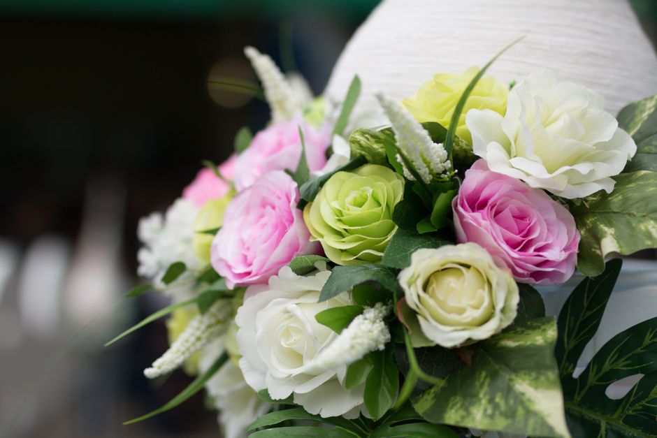 A close-up of a floral arrangement featuring a mix of fresh flowers including white roses, pink roses, and green eustoma, accented with white astilbe and lush green foliage. The bouquet is arranged in